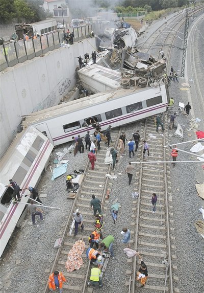 24日，救援人員在西班牙列車脫軌現(xiàn)場(chǎng)。一節(jié)車廂被強(qiáng)大的慣性拋上鐵道邊的高臺(tái)。