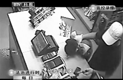 戴帽男子一手掐住加油站營業(yè)員，一手持發(fā)令槍指向另一營業(yè)員，要求“把錢給我裝起來”。