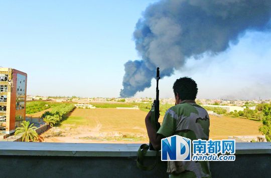 2日，利比亞首都的黎波里，一民兵武裝成員眺望被火箭彈擊中的儲(chǔ)油罐冒出濃煙。