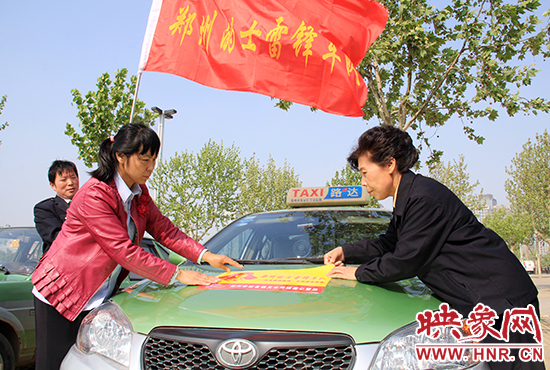 　　授旗結(jié)束后，首都的士雷鋒車隊(duì)王鳳進(jìn)隊(duì)長（右）與鄭州的的哥的姐在車身上貼上標(biāo)識(shí)。