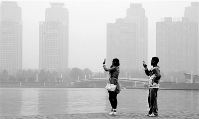 29日中午，鄭東新區(qū)如意湖畔，兩個年輕人拍攝霧霾中的景色。 鄭州晚報記者 馬健 圖