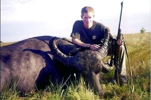哈里王子手持獵槍，蹲在一頭遭到獵殺的水牛旁邊