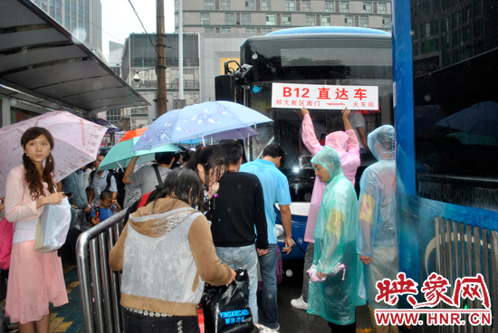 公交志愿者雨中高舉“B12-直達車”指示牌疏導返校學生乘車