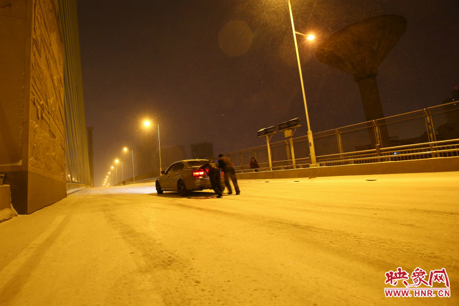 雪天路滑，汽車上橋打滑，兩名“推車人”幫助一輛私家車上坡。