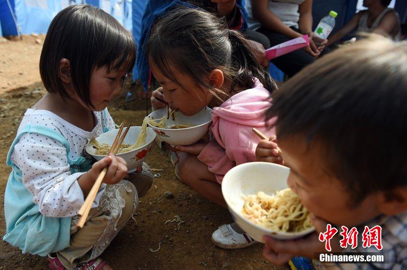 2014年8月6日，云南魯?shù)辇堫^山災(zāi)區(qū)，兒童在帳篷外吃飯。