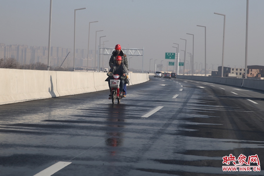 兩名工人騎車經(jīng)過灑水養(yǎng)護(hù)路面。