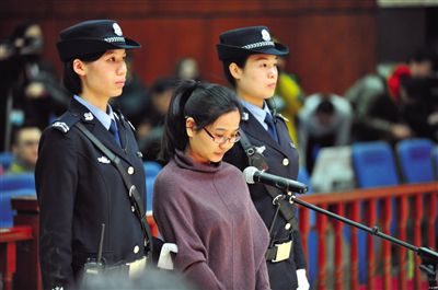被告人盧梅低著頭，站在朝陽法院刑事審判庭的被告席上。